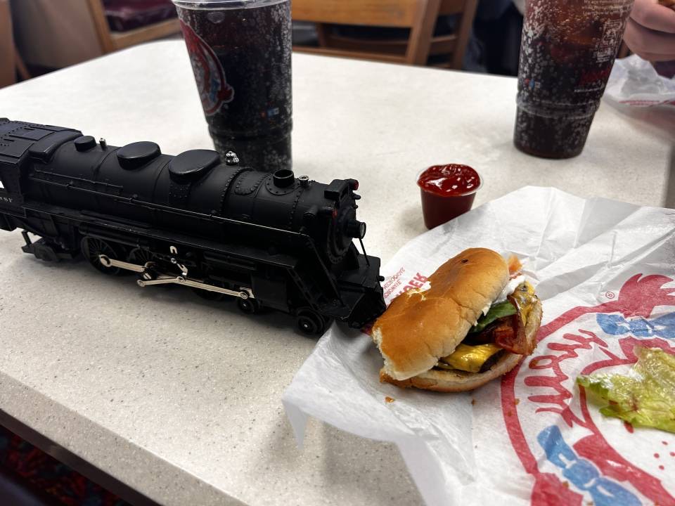 A photo of a toy train placed in a way that makes it look like its eating a burger.